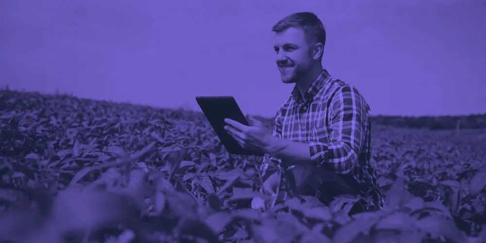 Productor sonriendo con una tablet en un campo de soja